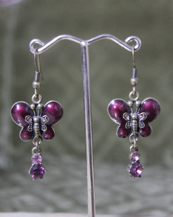 Butterfly-shaped earrings with purple gemstones on a stand against a blurred background